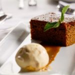 close up of sticky toffee pudding and ice cream on a white plate