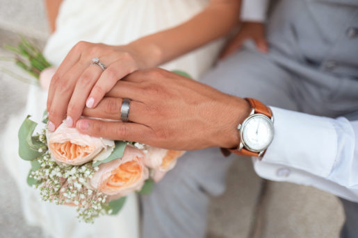 Newlyweds join hands over a bouquet, both wearing their rings