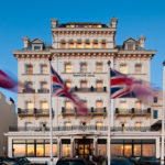 Exterior shot of Mercure Brighton Seafront Hotel with blurred Union Jack flags blowing in the wind, dusk, sunset reflection in windows