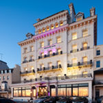 Exterior shot of Mercure Brighton Seafront Hotel with pink spotlights on hotel front, dusk, sunset reflection in windows