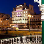 Exterior shot of Mercure Brighton Seafront Hotel with pink spotlights on hotel front at dusk, view from the seafront