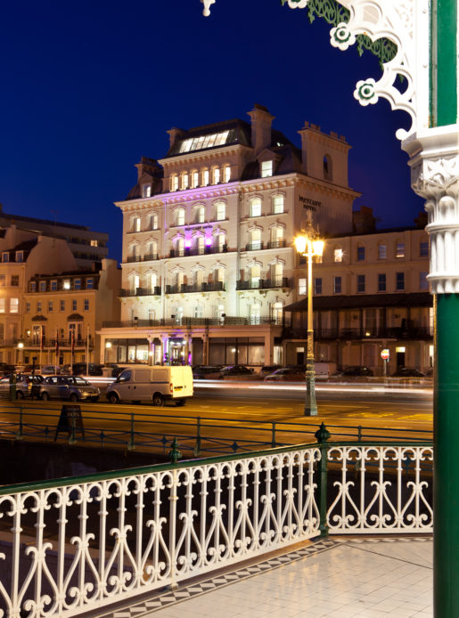 Exterior shot of Mercure Brighton Seafront Hotel with pink spotlights on hotel front at dusk, view from the seafront
